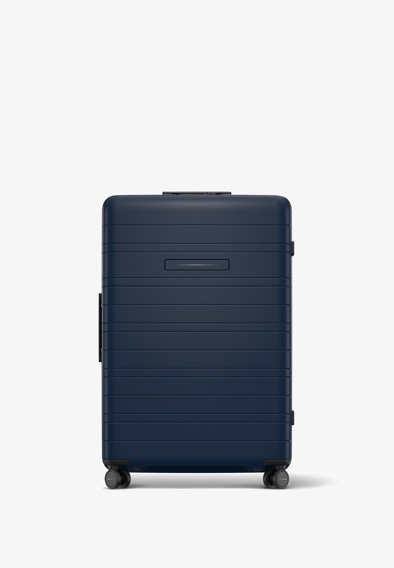 Valise rigide de couleur marine avec des rainures horizontales, une poignée rétractable et quatre roues. Dispose d'un emplacement pour une carte d'identité mince à l'avant.