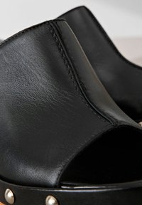 Sandali in pelle nera con apertura sulla punta, design curvato e cuciture in vista. Accentuati da borchie argento sulla suola.