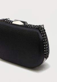 Czarna satynowa kopertówka o zaokrąglonym kształcie, z łańcuszkiem ozdobionym czarnymi koralikami oraz srebrnym zapięciem na górze.