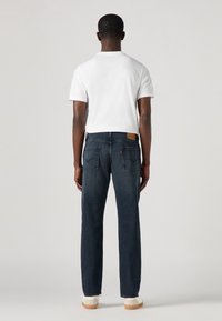 Mörkblå denimjeans med rak passform, sydda bakfickor och en läderetikett på midjebandet. Bärs med en vit t-shirt och sneakers.