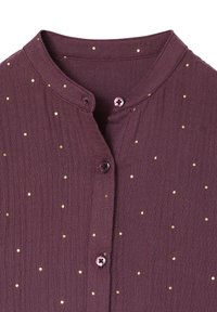 Lila Stoffhemd mit kleinen goldenen Punkten, einem runden Kragen und drei sichtbaren lila Knöpfen vorne.