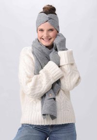 Grå, strikket pandebånd med et snoet design, parret med et matchende tørklæde og handsker, båret med en kraftig hvid kabelstrikket sweater.