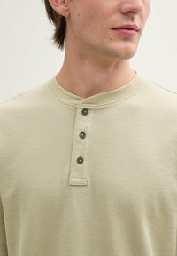 Koszulka w stylu Henley w jasnym beżu, z teksturowanej tkaniny, okrągłym dekoltem i czterema ciemnymi guzikami na listewce.
