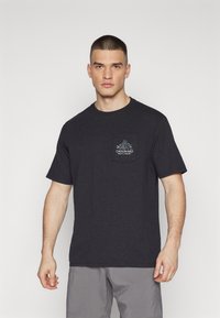 T-shirt en coton gris foncé avec un col rond, des manches courtes et une poche sur la poitrine arborant un logo de montagne et du texte.