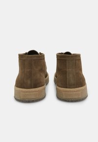 Bruine suède enkellaarzen met een structuurafwerking, voorzien van een beige rubberen zool en een achterlus, met een eenvoudig ontwerp en zonder zichtbare hardware.
