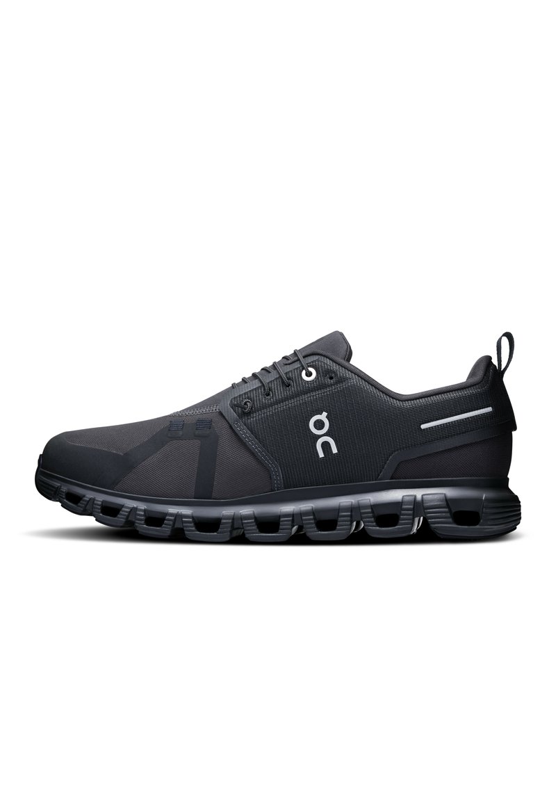 Baskets de sport noires avec une tige en maille, semelle en caoutchouc et un talon rembourré. Détail de logo notable et accents réfléchissants sur les côtés.