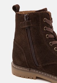 Hnědá semišová kotníková bota se zipem na boku, kulatou špičkou, kovovými očky na tkaničky a kontrastní podrážkou s texturovaným protiskluzem.