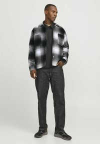 Black and white plaid shirt with a single chest pocket, worn over a dark t-shirt, paired with dark jeans and black sneakers.