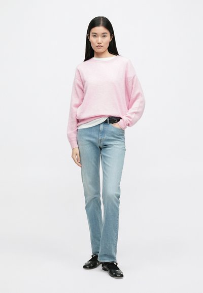 Sweatshirt rosa claro com ligeira textura, combinado com jeans azul claro e sapatos pretos de slip-on com embellishments. Design simples.
