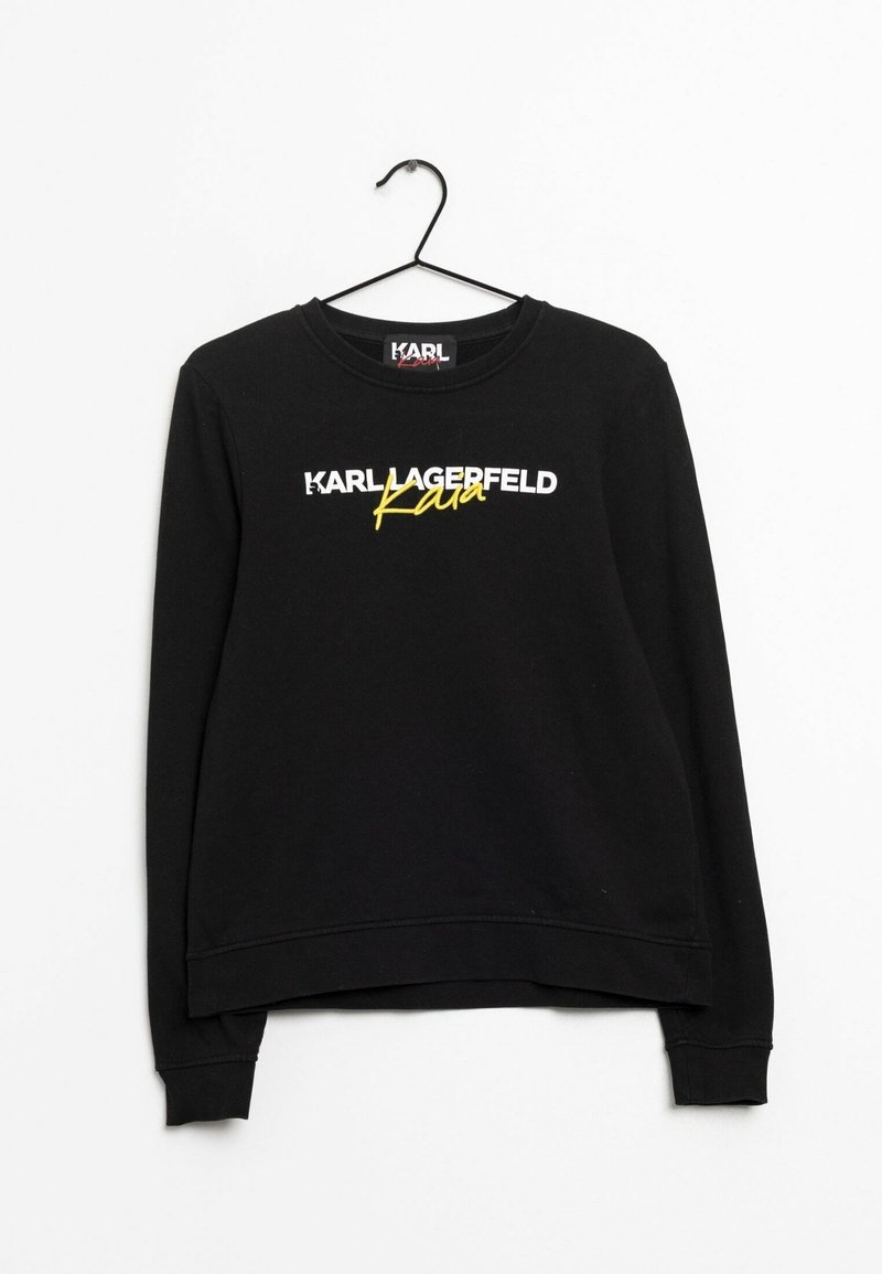 Černý dlouhý rukáv mikiny na ramínku se nápisem "KARL LAGERFELD" bílým písmem a "Kara" v žlutém ručně psaném písmu na přední straně.