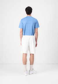 Heled sinise triibuga t-särk ja valged lühikesed püksid. T-särgil on ümmargune kaelus ning lühikestel pükstel on elastne vöökoht. Valged tossud lõpetavad riietuse.