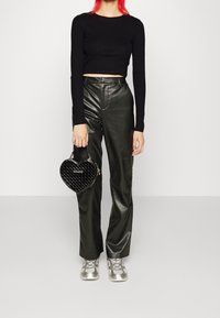 Schwarzes geripptes Cropped Top, hochgeschnittene schwarze Lederhosen, silberne Sneakers und eine schwarze gesteppte Handtasche in Herzform.