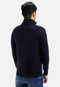 Pull noir marine avec un col montant, des poignets et un ourlet côtelés. Texture lisse avec une coupe ajustée pour la chaleur et le confort.