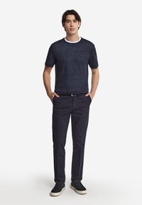 Marinblå t-shirt med kort ärm och vit rund hals, kombinerad med marinblå chinos och marinblå sneakers med vita sulor. Slät textur, avslappnad design.