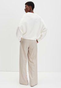 Maglione bianco cropped con vestibilità rilassata, abbinato a pantaloni a vita alta di un beige chiaro; tessuto morbido e linee pulite.