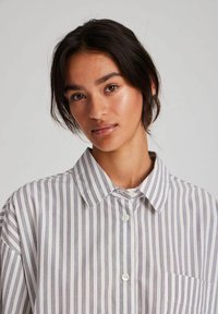Striped button-up shirt made of lightweight fabric, featuring vertical navy and white stripes, a collar, and a single chest pocket.