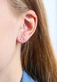 Boucle d'oreille en argent en forme de croissant de lune présentée sur un lobe, avec une finition polie et un design simple sur fond clair.