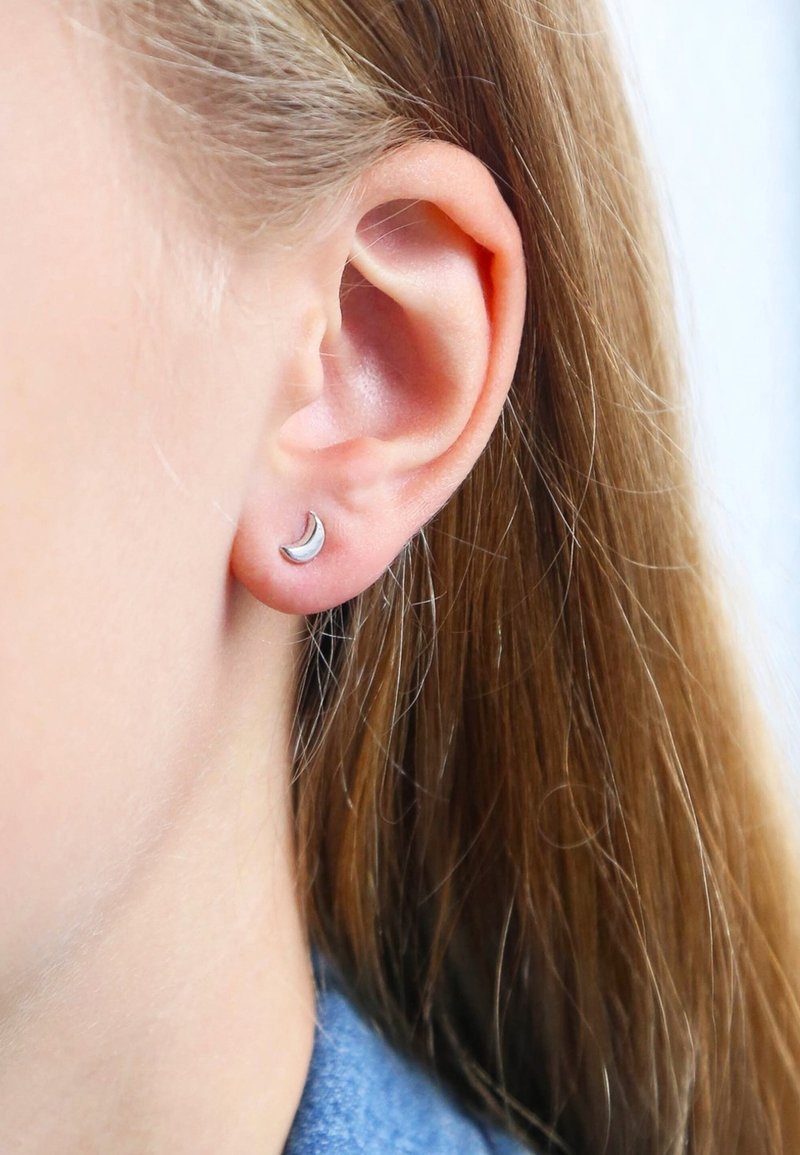 Boucle d'oreille en argent en forme de croissant de lune présentée sur un lobe, avec une finition polie et un design simple sur fond clair.