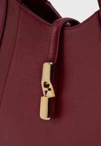 Tamno crvena teksturirana kožna torba s detaljem zlatnog kopčanja na prednjem remenu.