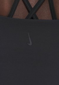 Haut de sport noir avec une texture lisse, des bretelles noires croisées dans le dos, et un petit logo Nike discret dans le coin inférieur.