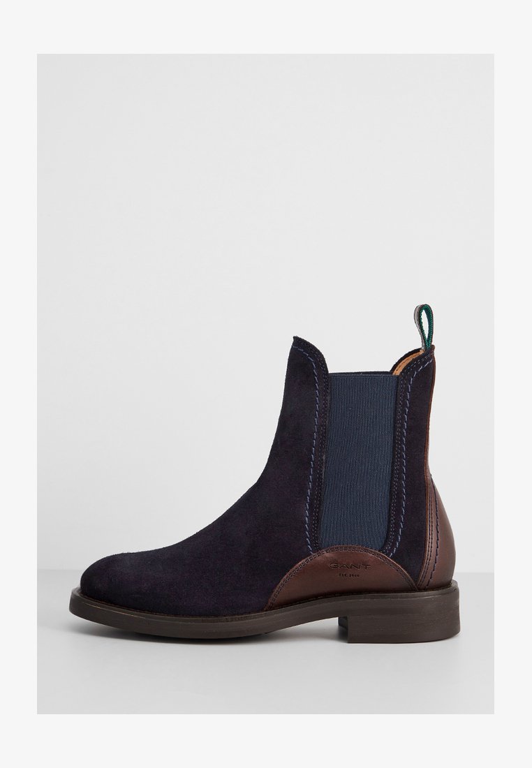 Suede Chelsea boot in dark navy with contrasting brown leather accents. Features elastic side panels and a green heel pull tab. Flat sole.
