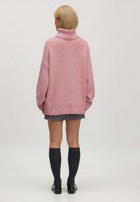 Roze oversized trui met een hoge kraag, geribde manchetten en zoom. Draagt over een grijze rok met knielange donkergrijze socks en zwarte schoenen.