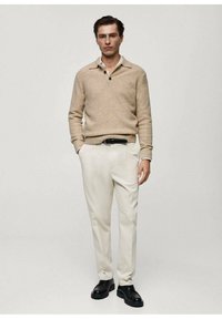 Maglione beige a maglia con colletto e tre bottoni, abbinato a pantaloni crema e scarpe in pelle nera. Tessuto liscio e vestibilità sartoriale.