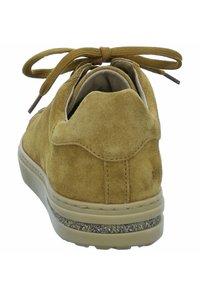 Scarpa in scamosciato giallo-bruno con punta rotonda, suola piatta e lacci marroni. Presenta un colletto imbottito e un'accento testurizzato sulla suola.