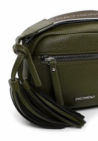 Olive green leather crossbody bag with a textured finish, silver hardware, frontal zipper pocket, and a decorative tassel detail.