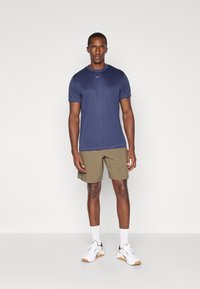 Navy blue athletic t-shirt, short sleeves, paired with olive green shorts. Model wears white sneakers with black accents and white socks.