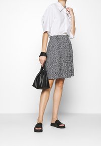 Valkoinen lyhythihainen paita, kuvioitu laivastonsininen hame, musta laukku ja sandaalit. Hameessa on kukkakuvio, ja laukussa on kerätty muotoilu.