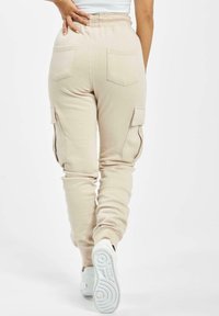 Béžové cargo tepláky s elastickým pasem, zadními kapsami a bočními kapsami. Měkká látka, zúžený střih a žebrované manžety na kotnících.