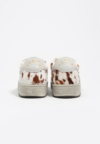 Niskie sneakersy z wierzchem z brązowego i białego futra w plamki, szarym skórzanym elementem na pięcie oraz teksturowaną szaro-rubberową podeszwą z brandingiem.