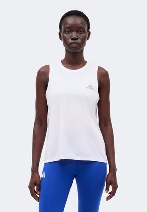 Femeie în picioare cu fața înainte, purtând un top sport alb fără mâneci și colanți albastru strălucitor cu logo-urile brandului vizibile pe ambele.