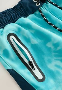 Shorts de bain en tissu avec un motif tie-dye turquoise, dotés d'une poche zippée avec des accents noirs et d'une taille à cordon.