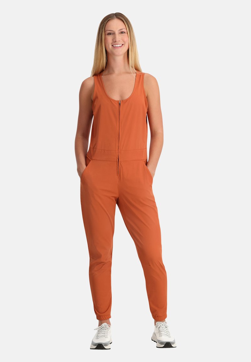 Tuta arancione con zip frontale, scollatura a barchetta, due tasche laterali e gambe affusolate; realizzata in tessuto liscio ed elastico.