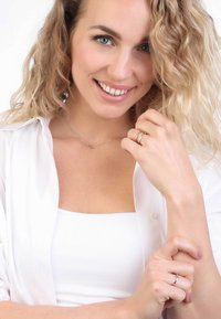 Zilveren sieraden met een delicate ketting en een minimalistische hanger, gedragen met een witte top. Zacht, golvend haar en een natuurlijke uitstraling verhogen de helderheid.