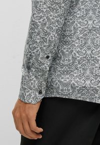 Camisa de manga larga con un patrón cachemira en blanco y negro, textura suave, puños con botones y dobladillo curvado.