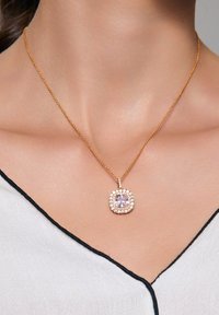 Złota naszyjnik z kwadratowym wisiorkiem, zdobionym centralnym różowym kamieniem otoczonym pierścieniem błyszczących przezroczystych kamieni.