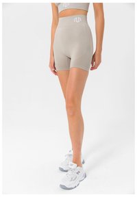 Beige høy midje shorts med teksturert design, tettsittende silhuett og subtil logo-detall. Kombinert med hvite joggesko.