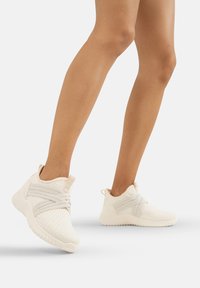 Zapatillas de punto blancas con un upper texturizado, correas elásticas cruzadas y una suela de goma. Presentan un collar acolchado y una lengüeta trasera para tirar.