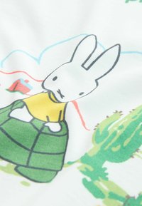 Bombažna tkanina z ilustracijo zajčka v rumeni majici in zeleni lupini, obdanega s kaktusi in igrivimi vzorci v mehkih barvah.