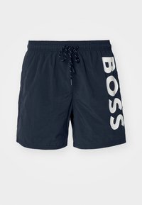 Sötétkék strandnadrág könnyű anyagból, rugalmas derékkal, zsinóros záródással és nagy fehér "BOSS" logóval az oldalon.