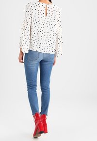 Blusa bianca con pois neri e maniche a campana, con scollatura a chiave sul retro, abbinata a jeans skinny blu e ankle boots rossi lucidi.