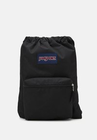 Sac à dos noir en tissu durable avec un haut resserré. Comprend une poche zippée à l'avant et un patch logo Jansport bleu et rouge.
