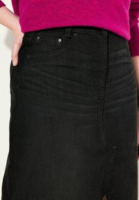 Jupe en denim noir à taille haute, avec une texture lisse, des coutures subtiles et des poches devant, associée à un pull rose vif.