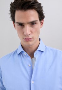 Cămașă albastru deschis cu nasturi, realizată dintr-un material neted, cu guler ascuțit și textură subtilă, având nasturi albi.