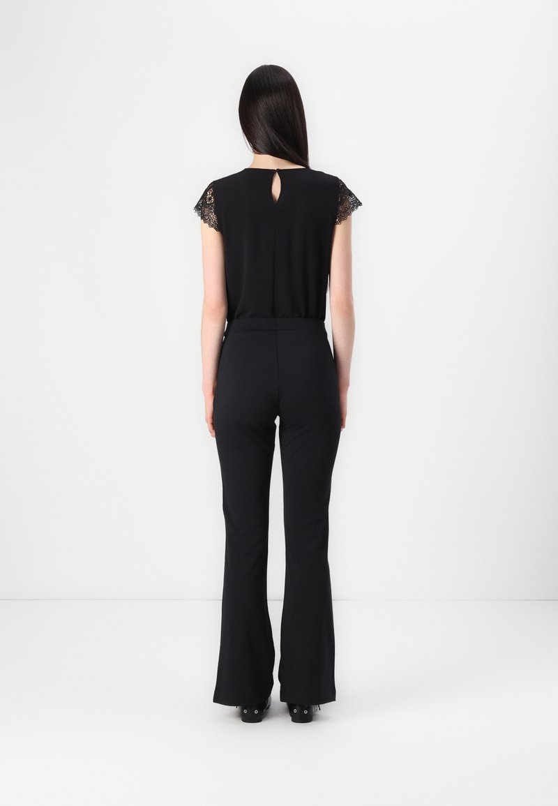 Schwarzer Jumpsuit mit Spitzenbesatz an den Ärmeln und einem Schlüssellochdetail im Rücken, ausgestellt am Bein und tailliert. Glatte Stoffstruktur.