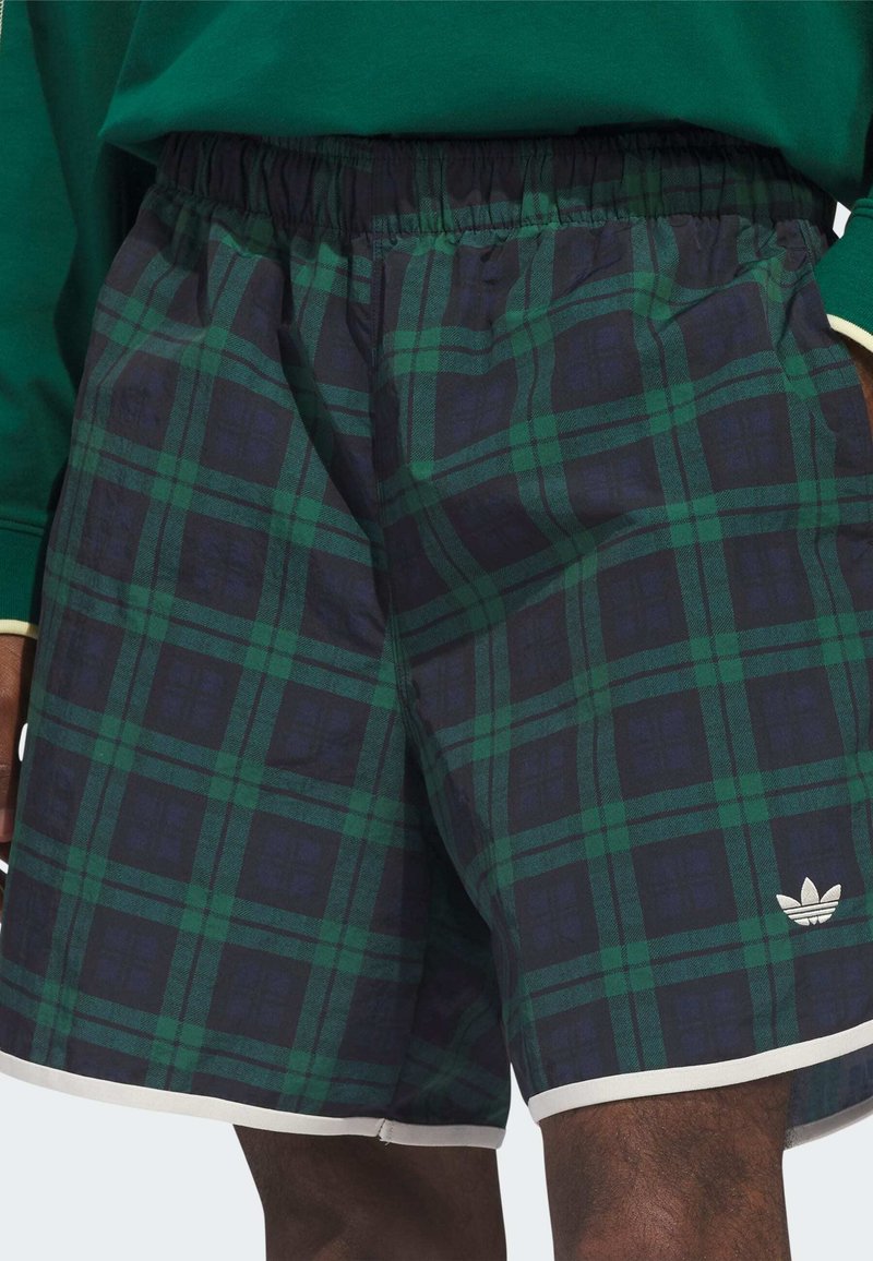 Grün-navy karierte Shorts aus Stoff mit elastischem Bund und weißem Besatz, versehen mit einem Adidas-Logo unten rechts.