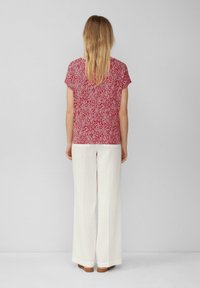 Rood gestreept top met korte mouwen in combinatie met witte broek. Het topje heeft een geometrisch ontwerp; de broek heeft een losse, vloeiende pasvorm in een textuurstof.